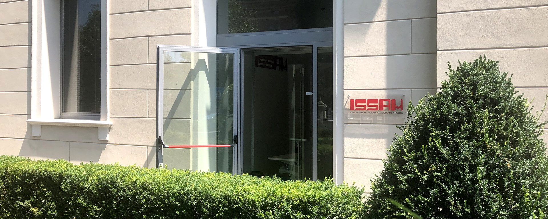 entrata di una struttura con siepi e la targa con logo ISSAM in rosso appesa all'entrata