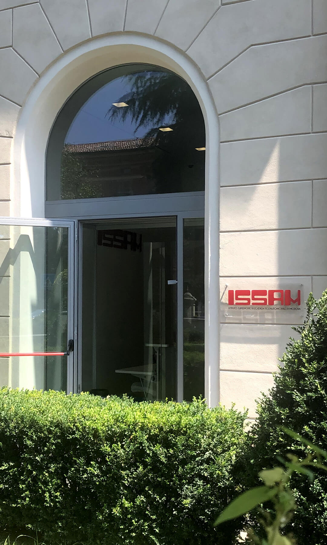 entrata di una struttura con siepi e la targa con logo ISSAM in rosso appesa all'entrata