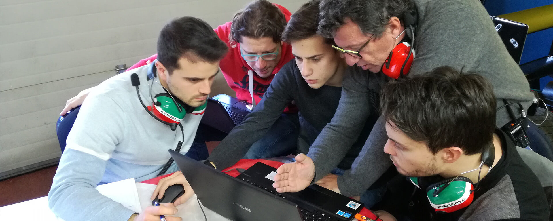 Young students and teachers wear headsets with microphones and look at a computer screen