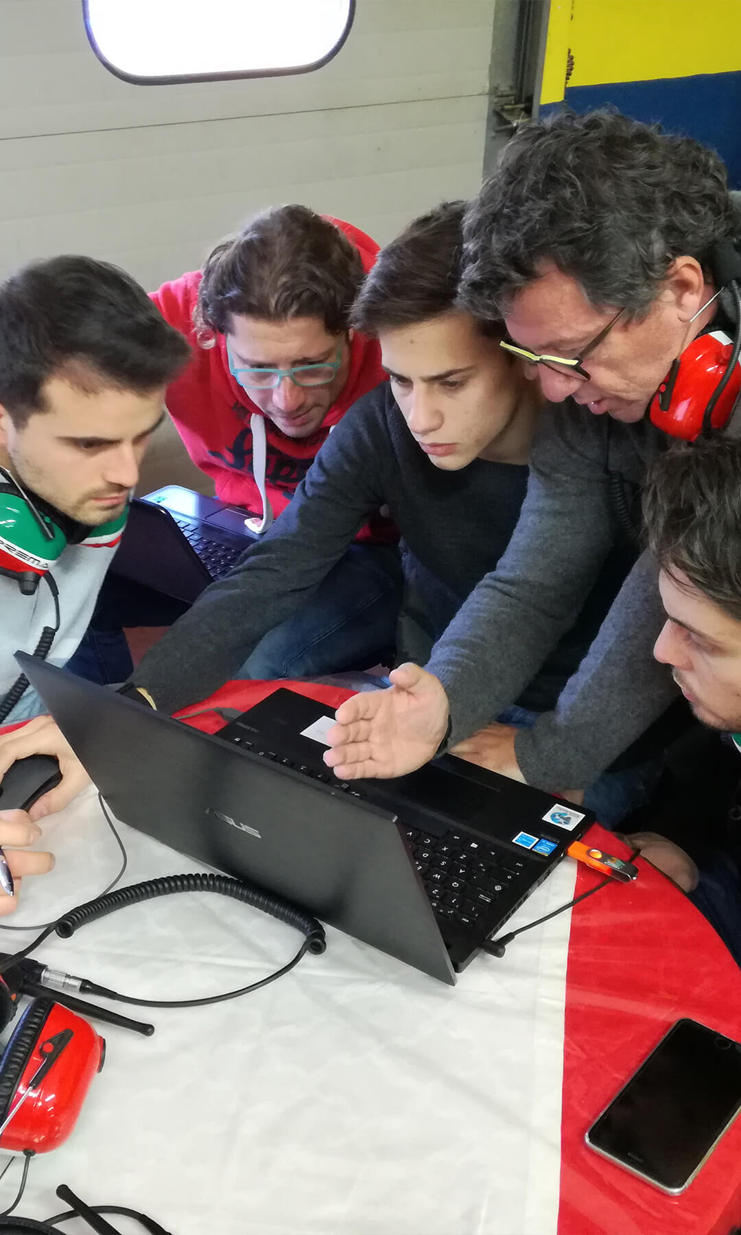 Young students and teachers wear headsets with microphones and look at a computer screen