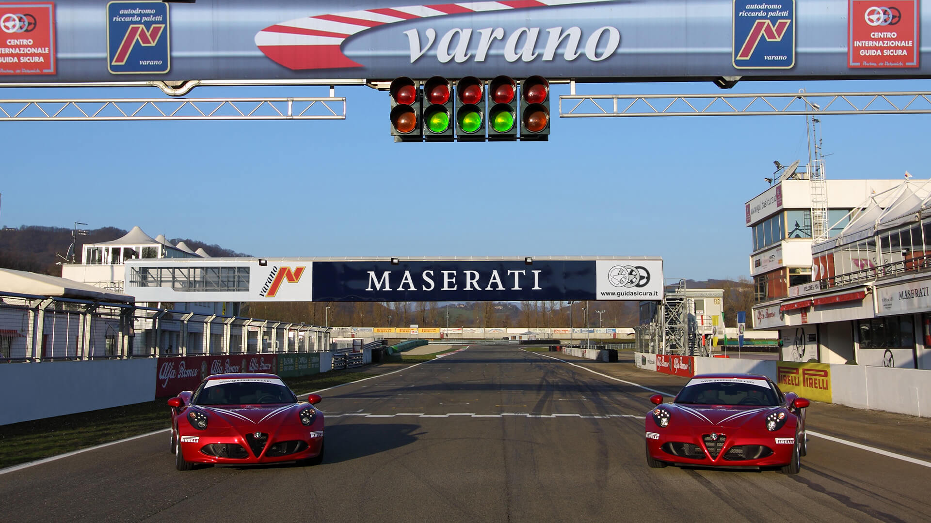 due alfa romeo 4c rosse parcheggiate sulla linea di partenza del circuito dell'autodromo di varano, con il cartellone maserati alle spalle