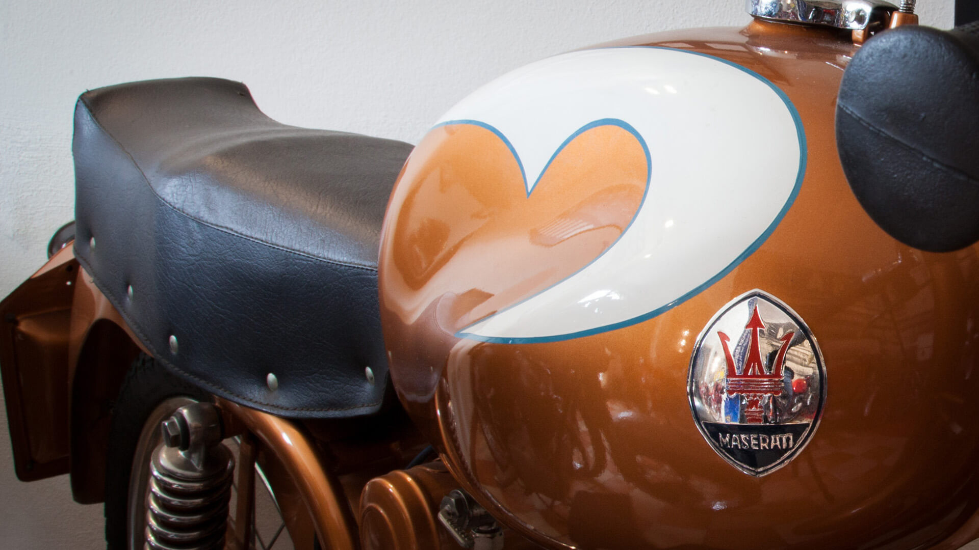 dettaglio di logo maserati su moto d'epoca color bronzo con disegno bianco e sellino in pelle nera