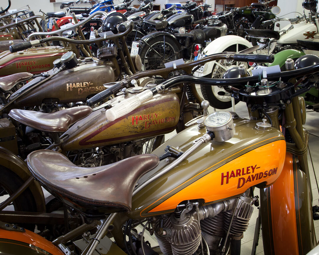 Una serie di harley davidson da collezione una parcheggiata affianco all'altra, tra altre moto della collezione battilani