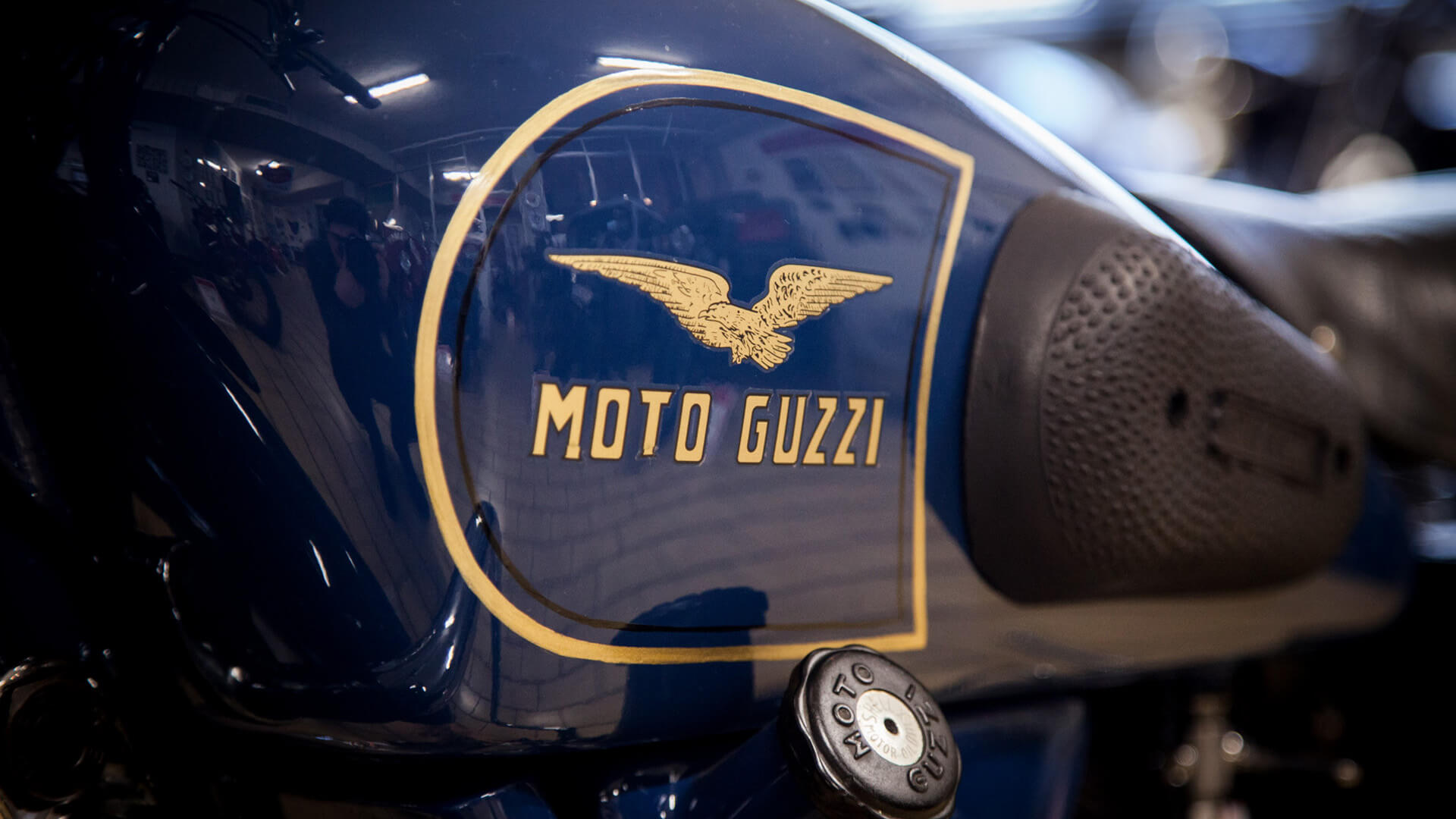 close up of moto guzzi logo written in gold eagle on blue motorcycle