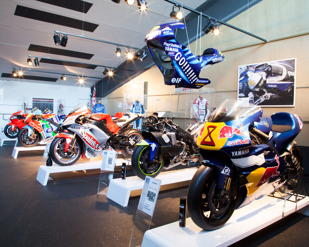 Inside the poggi collection, several yamaha models with unique racing liveries are on display, the room is illuminated and on the walls are memorabilia, racing suits and historical photos