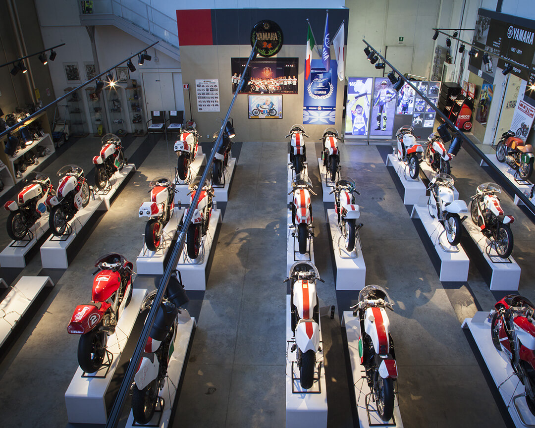 View from the other side an exhibition room of the poggi collection, where several yamaha motorbikes from the history of motorcycling are present, on the walls are posters and motorcycling memorabilia