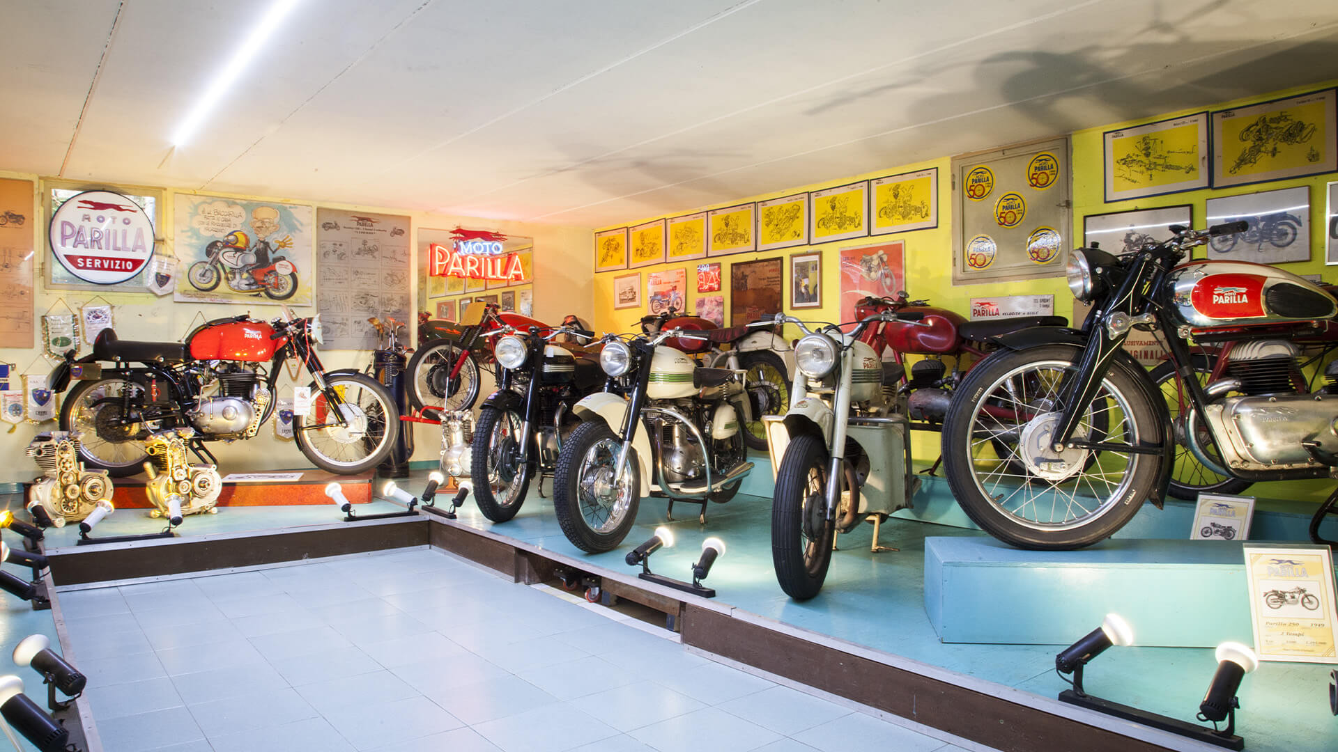 Lighted Moto Parilla exhibition hall with several collectible motorcycles, engines and vintage posters inside.