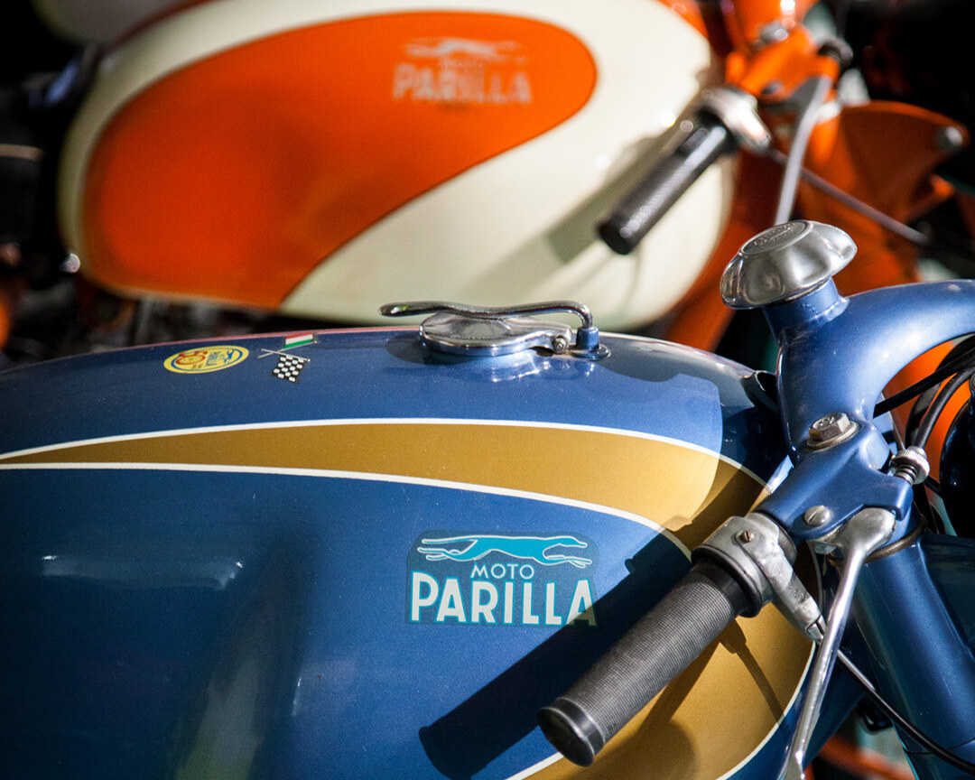 detail of the “moto parilla” logo on the tank of a vintage motorcycle, where you can also see the handlebars and two other stickers