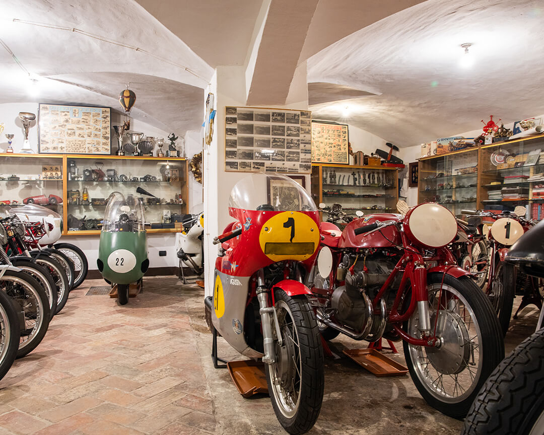 Inside a display room of the Parmeggiani collection, with trophies and memorabilia on the wall, are many vintage motorcycles with unique colors, liveries and fairings.