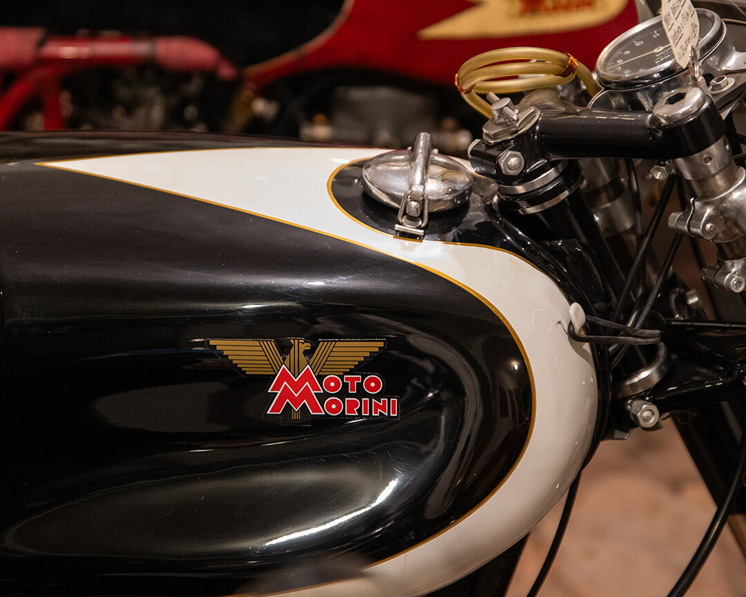 Detail of a guzzi motorcycle tank, from the Parmeggiani collection. the coloring is black and white with the moto guzzi logo in the foreground