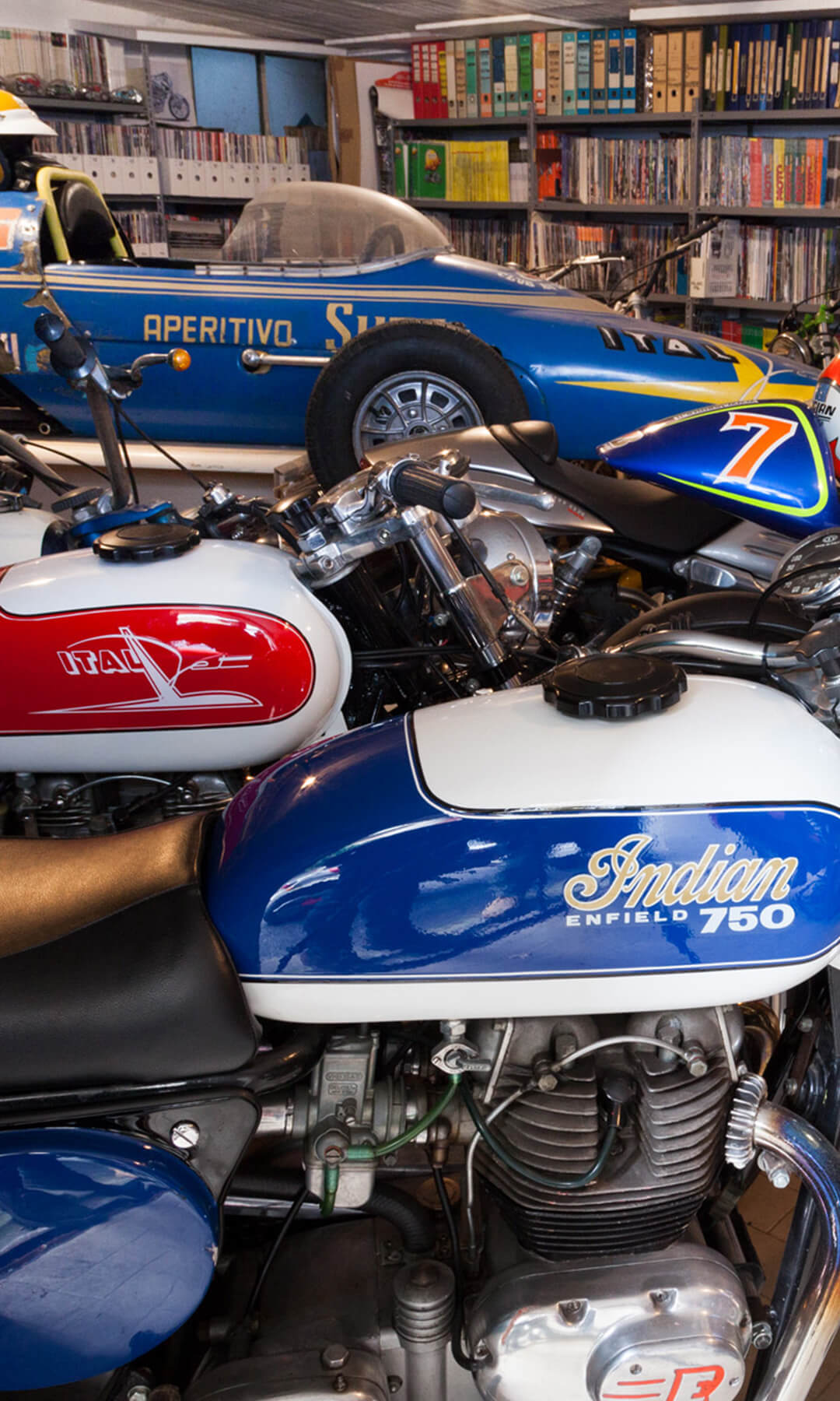 Inside the Mesto collection is a room full of files and memorabilia, with vintage motorcycles and a blue single-seater collector's car in the foreground.