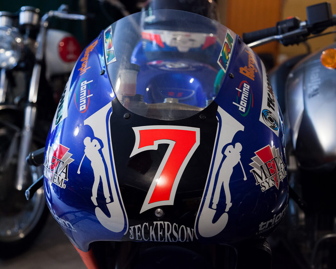 Muzzle of a vintage racing motorcycle, prominently featuring the number 7 and various sponsors. The motorcycle stands alongside other collectibles from the Pasquale mesto collection