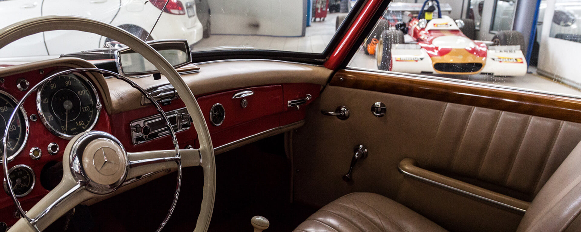 From inside the cockpit of a vintage mercedes, part of the Pollini workshop can be seen, where a single-seater racing car can be seen