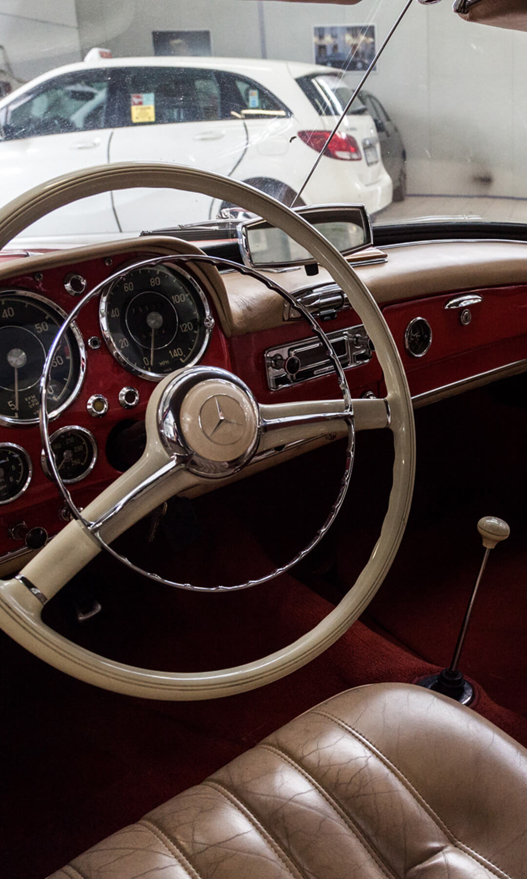 From inside the cockpit of a vintage mercedes, part of the Pollini workshop can be seen, where a single-seater racing car can be seen