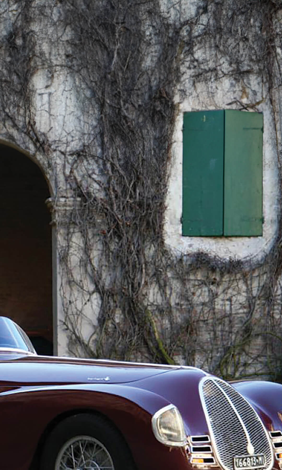 A vintage convertible car of those burgundy, from the righini collection, parked in front of an old building