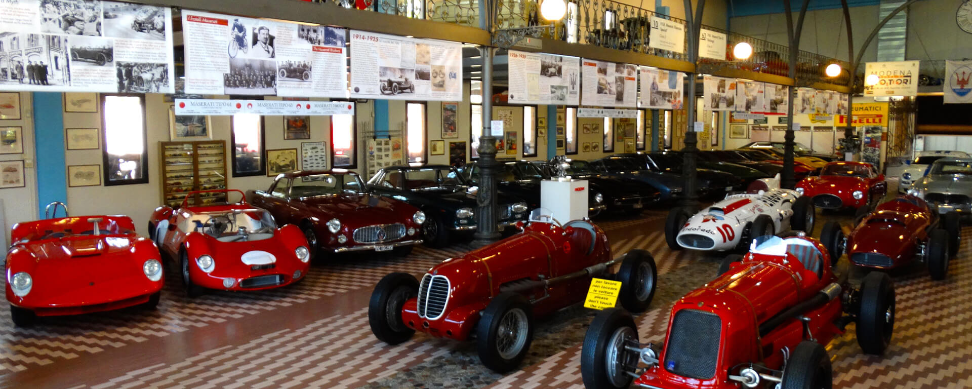 Sala espositiva della collezione umberto panini con al suo interno diverse auto da d'epoca e cimeli automobilistici, appesi al soppalco cartelloni sulla storia maserati