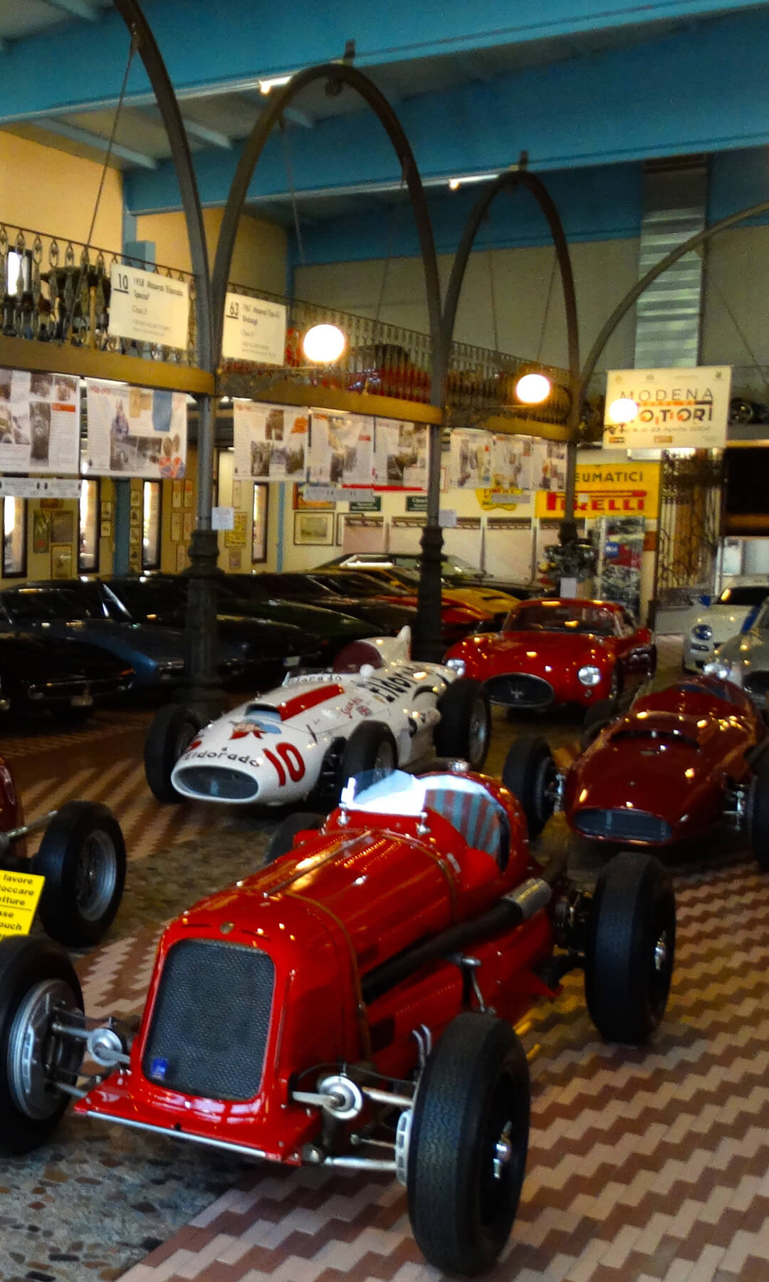 Sala espositiva della collezione umberto panini con al suo interno diverse auto da collezione e cimeli automobilistici, appesi al soppalco cartelloni sulla storia maserati