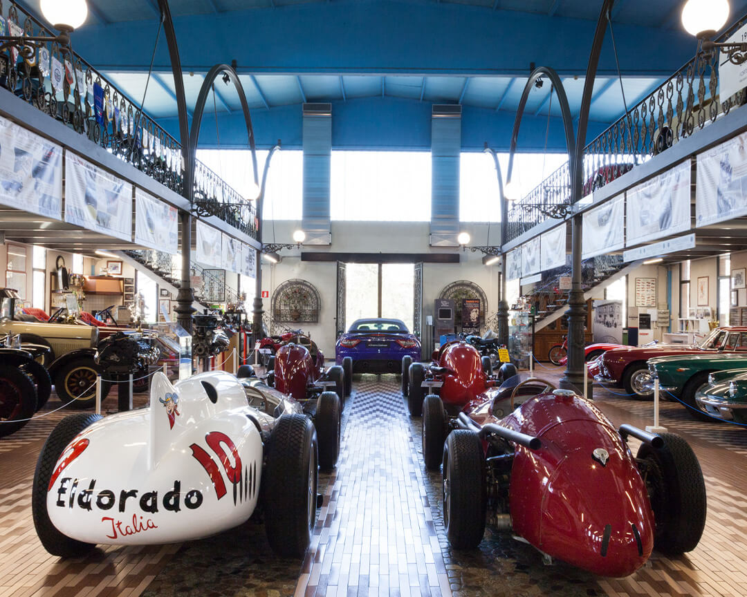 Dal fondo della sala principale della collezione umberto panini, sono fotografate diverse auto d'epoca maserati, tra cui quattro monoposto da collezione