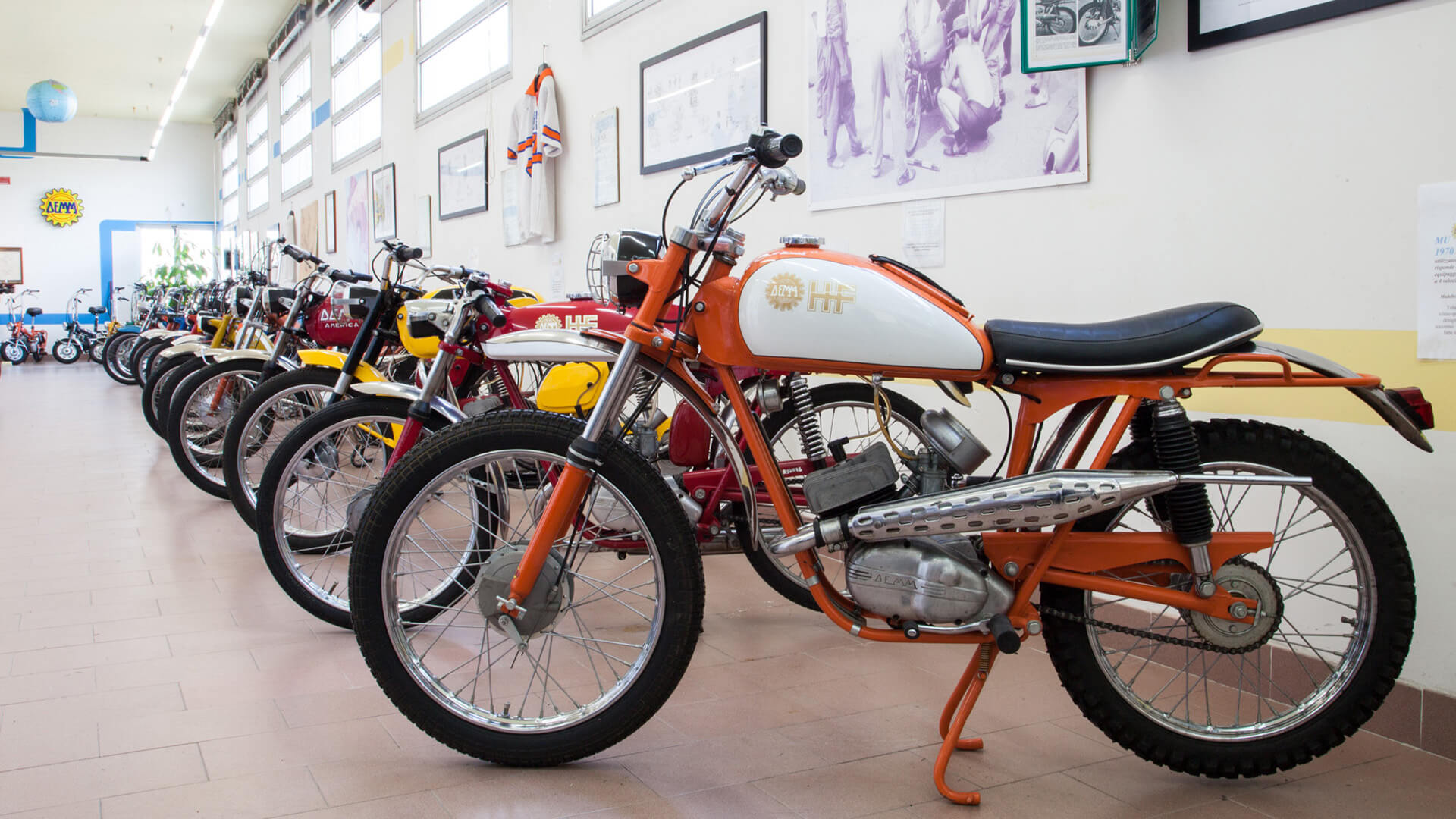 Vista laterale di una serie di moto d'epoca Demm, all'interno dell'omonimo museo. Sulle pareti cimeli e foto della storia Demm