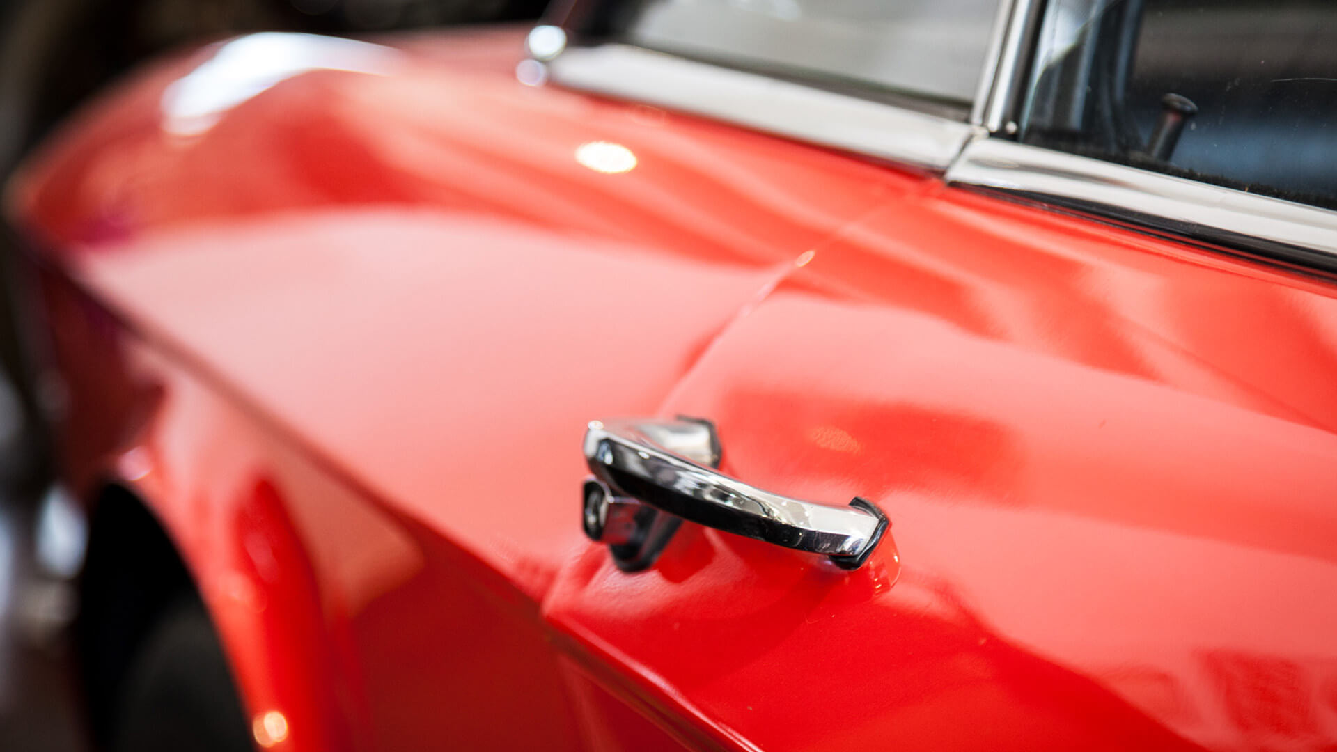 Handle of a vintage car door, in red paint, the car is part of the automobile museum collection