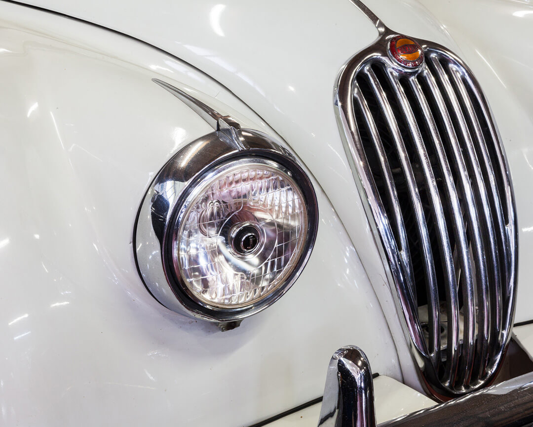 Detail of the headlight and grille of a vintage jaguar, in white paint from the automobile museum collection
