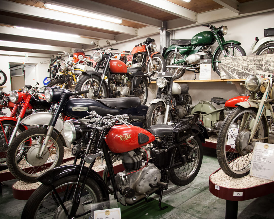 Several collector's motorbikes are positioned inside an exhibition room of the National Motorcycle Museum. The motorbikes are parked side by side and there are also motorbikes, with special fairings, on the walls
