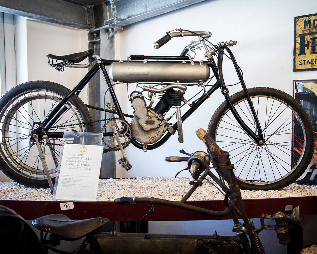 Side view of a very old motorbike, including pedals and bike frame. The vehicle is inside the National Motorcycle Museum