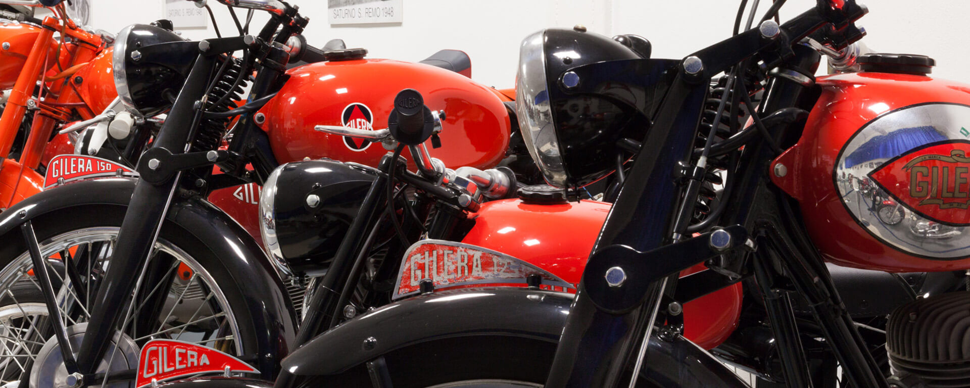 a series of gilera motorbikes parked side by side in black and orange inside the bariaschi museum