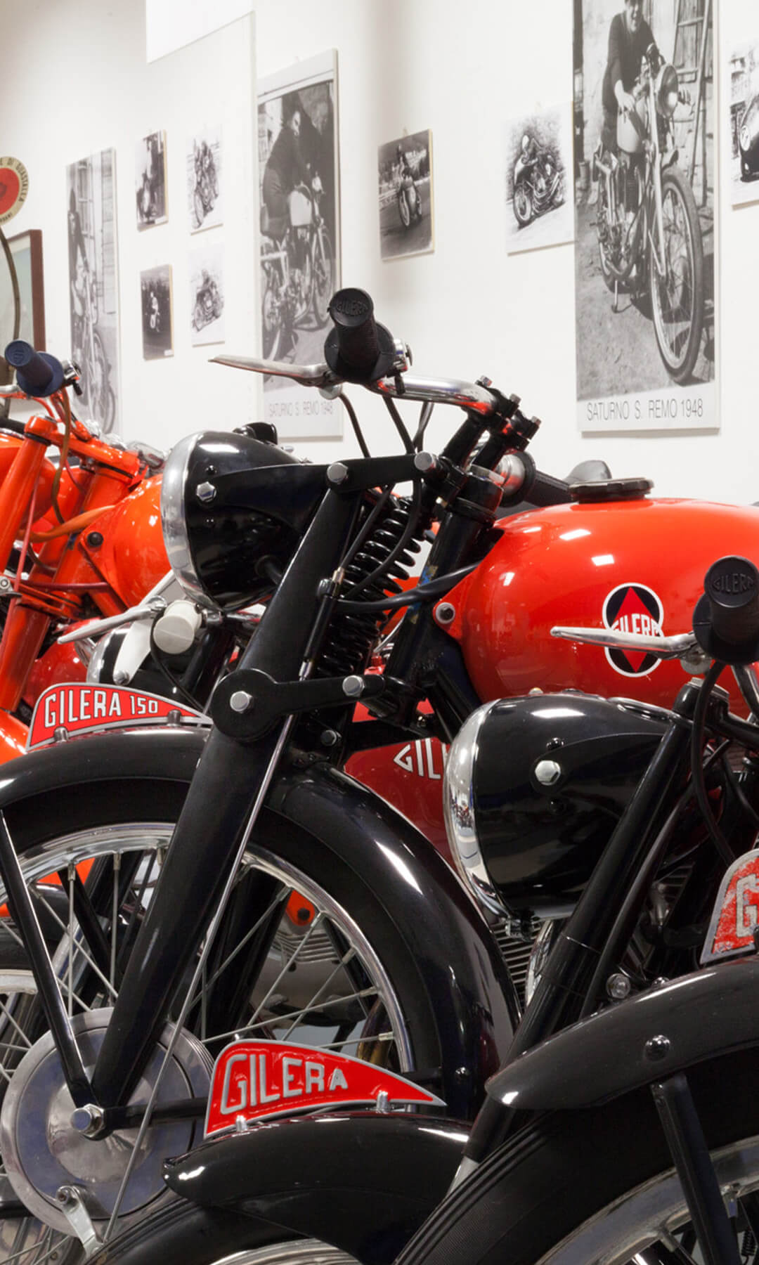 a series of gilera motorbikes parked side by side in black and orange inside the bariaschi museum