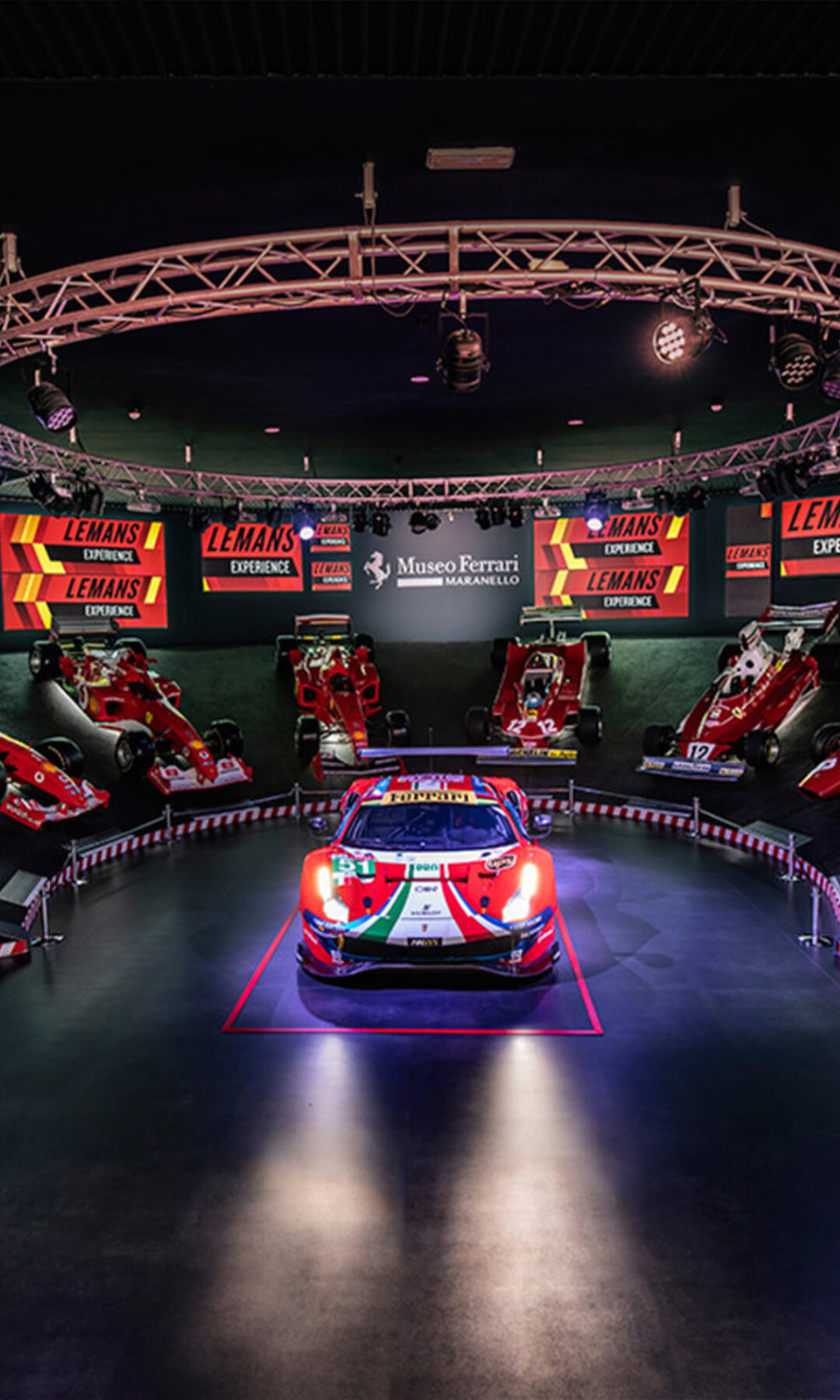 sala del museo Ferrari a Maranello con auto sportiva al centro e attorno diversi veicoli di formula 1 dal più antico al più recente