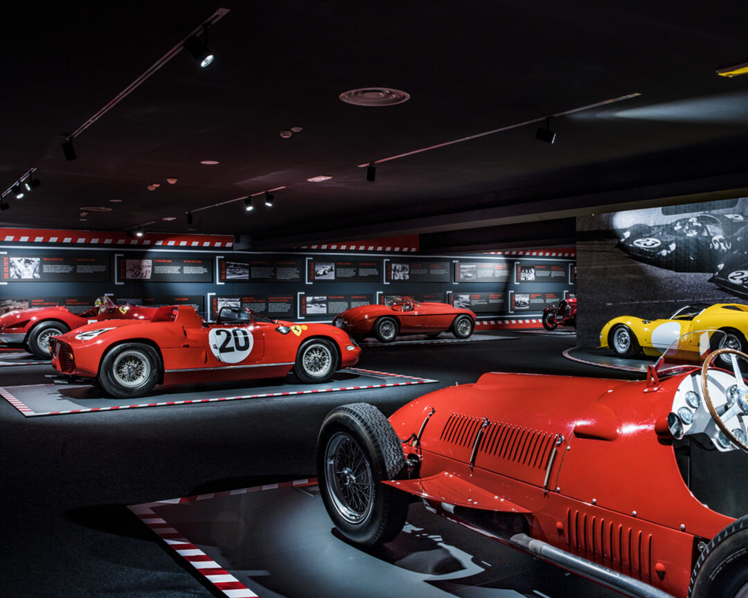 in one of the rooms of the ferrari maranello museum, you can see several vintage ferrari racing models, with photos and descriptions of the cars on the walls