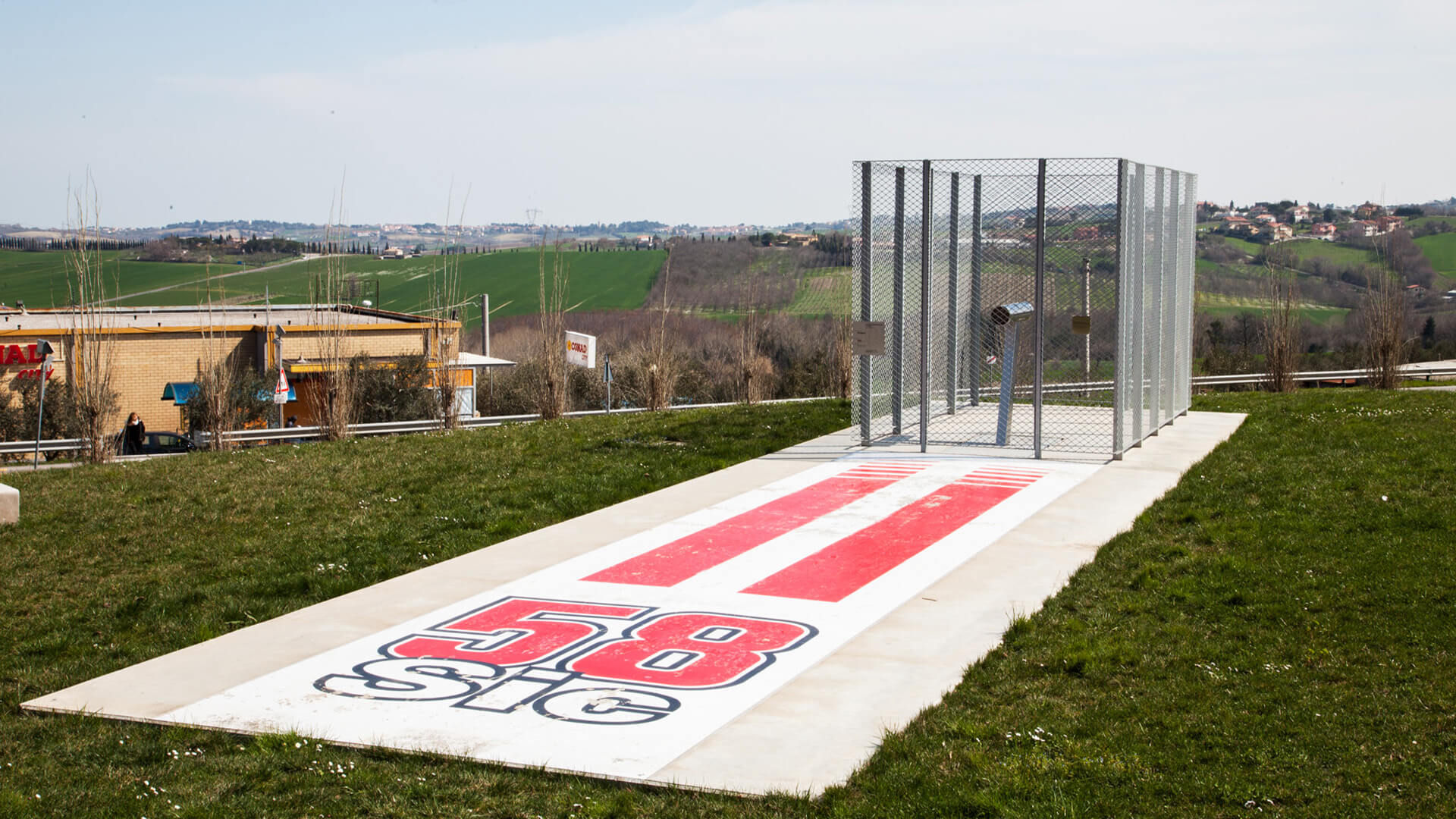 piattaforma in legno con scritta 58 SIC e struttura con rete all'aperto e tutto intorno campagne