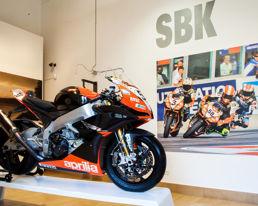 moto numero 58 appartenente a Marco SImoncelli nera e rosso con logo Aprilia e Pirelli a destra una foto attaccata al muro di una corsa di MotoGP