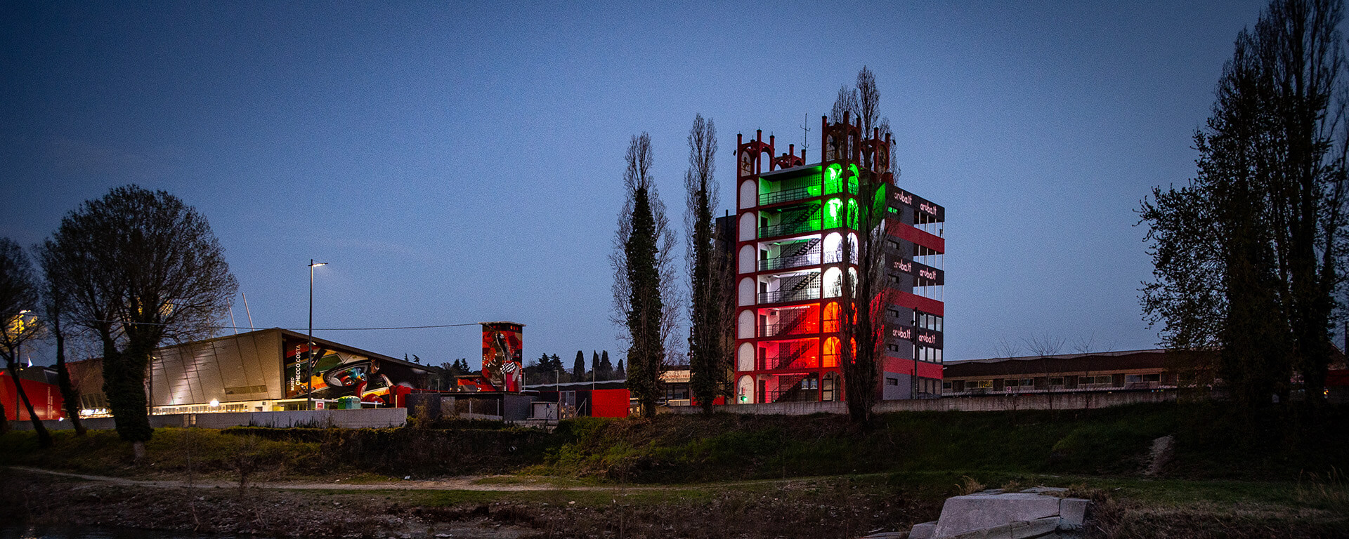 front view of a 7-story building that with light effects simulates the Italian flag and next to it the Checco Costa Imola Autodrome Multimedia Museum