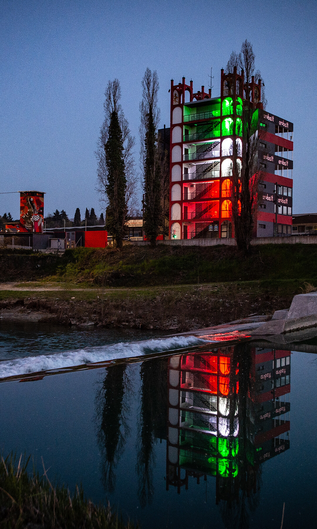 front view of a 7-story building that with light effects simulates the Italian flag and next to it the Checco Costa Imola Autodrome Multimedia Museum