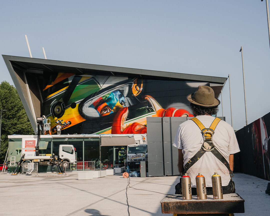 graffiti of a pilot where only the helmet and eyes can be seen and from behind one of the artists with 3 cans of paint