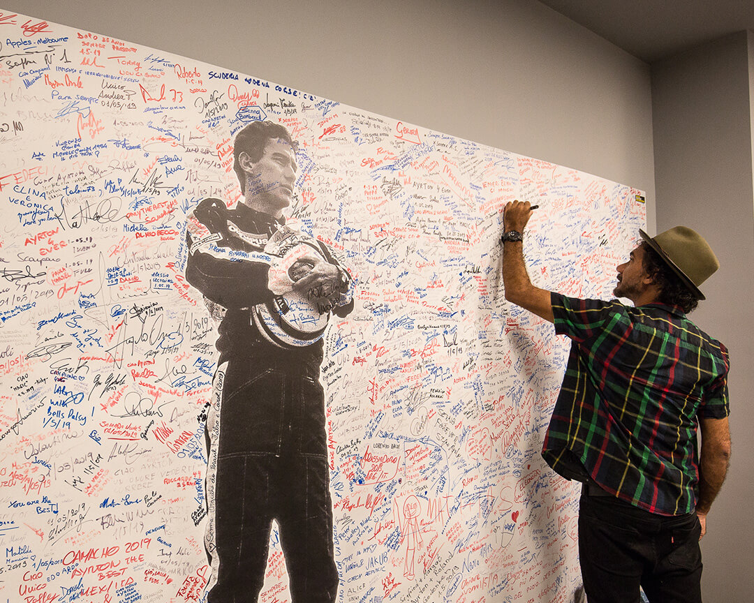 photo of Ayrton Senna hanging in a room with signatures and a person who is signing the photo