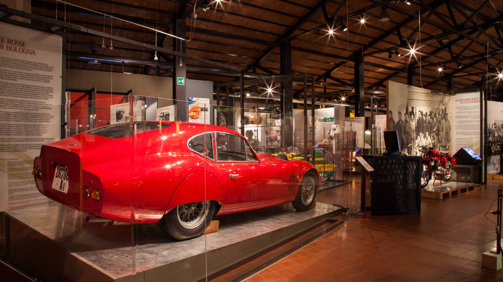 Vintage car, red, displayed in a glass case. The car has an aerodynamic shape, with a design typical of classic sports cars, probably from the 50s or 60s.