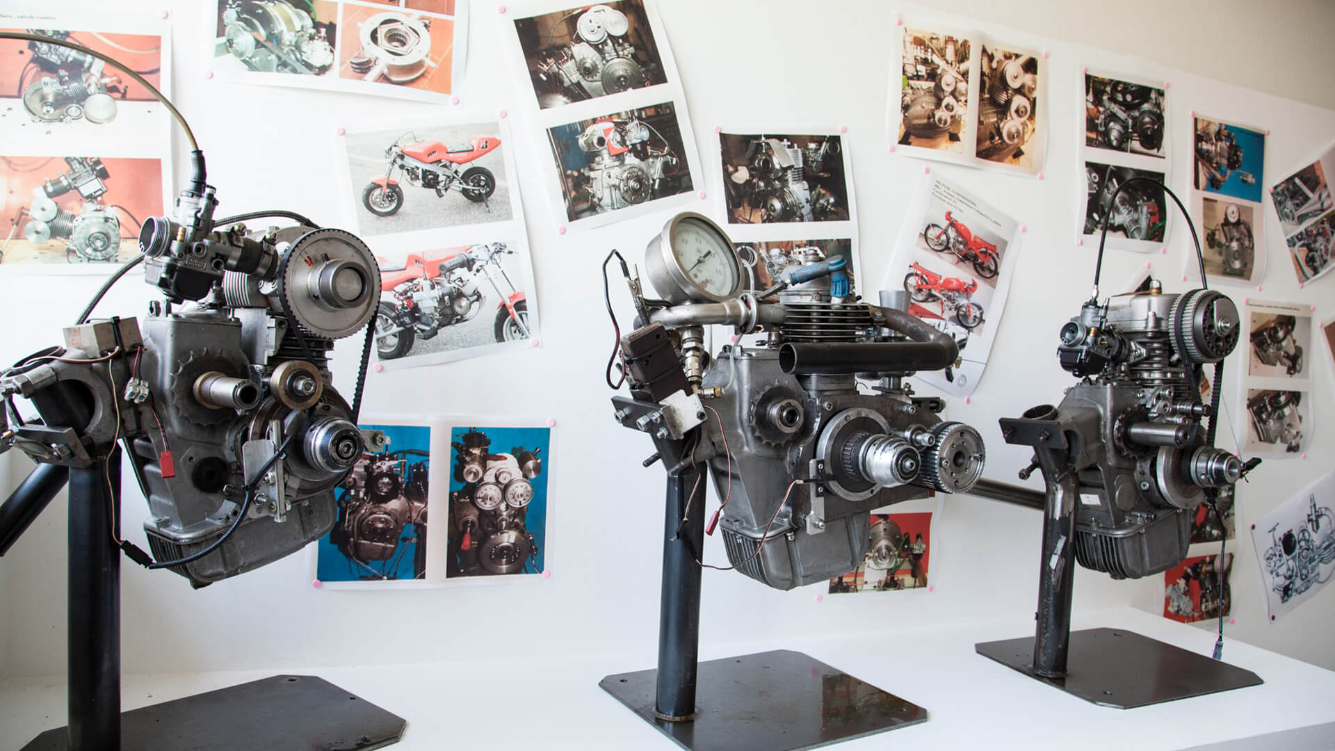 three motorcycle engines, displayed in the motorcycle museum in scortichino, with several vintage photos on the wall depicting the same engines and collectible way