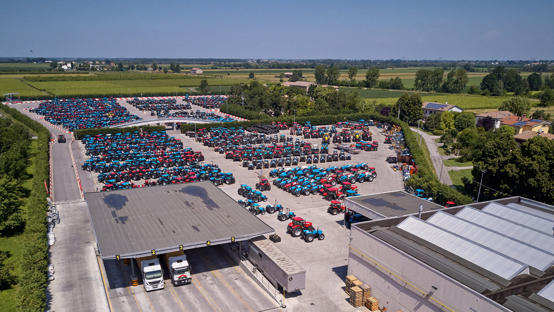 Aerial view of the argo tractos factory and industrial parking lot, where dozens of tractors and a couple of shipping trucks are parked