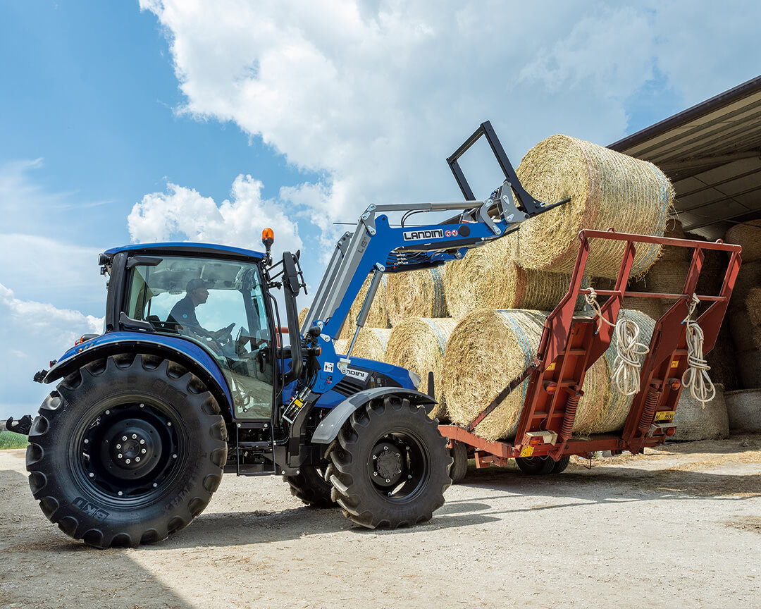 an argo tractor tractors skims hay bales from the trailer of a truck