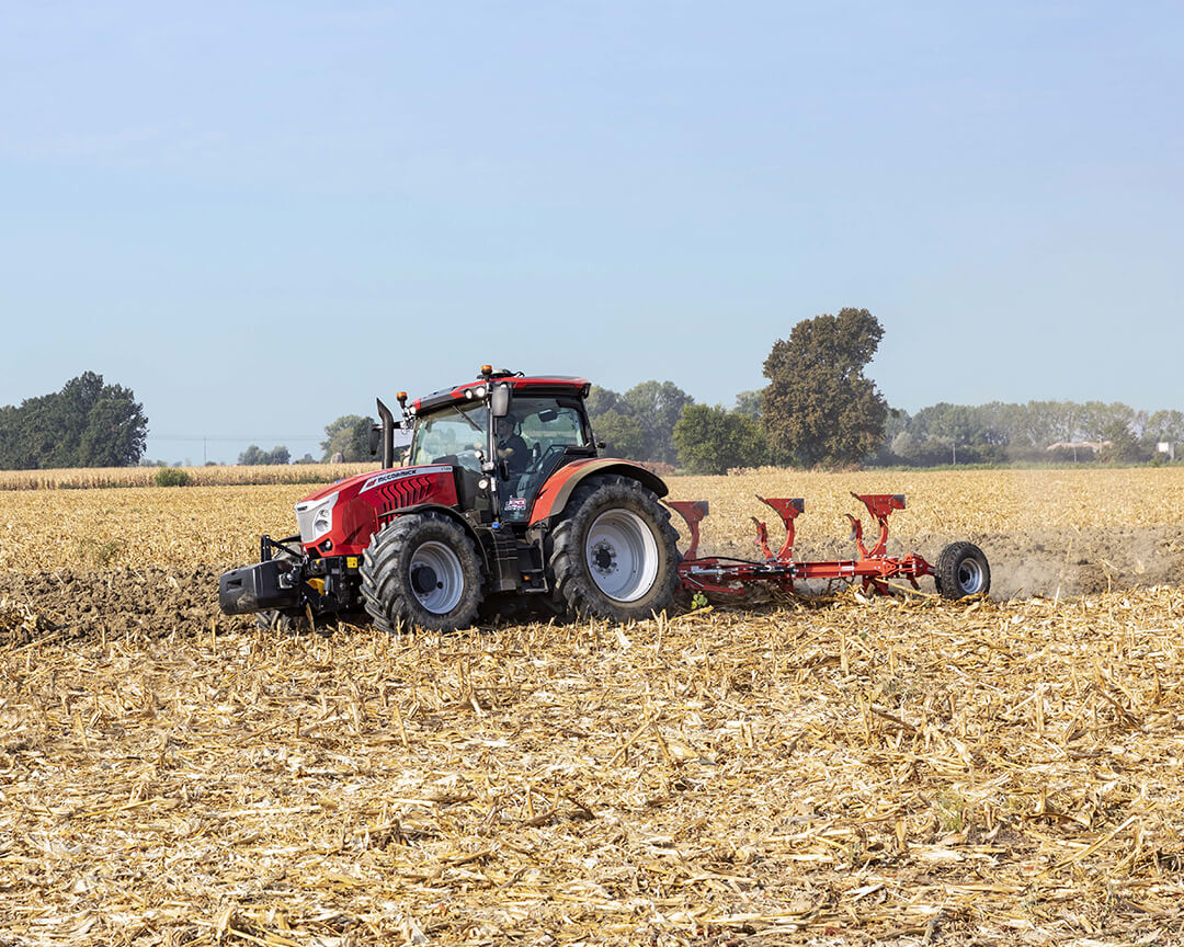 A red argo tractors tractor, working on a field using a plow