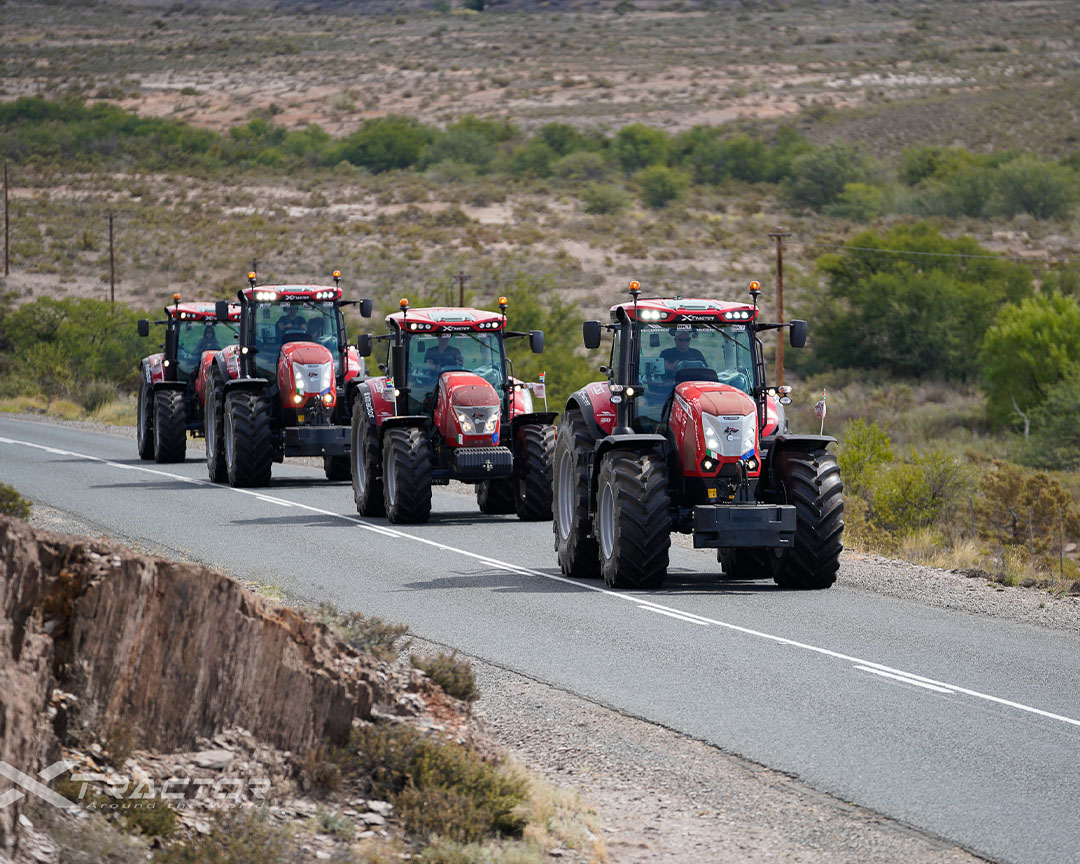 Four red argo tractors traversing a country road, with headlights on