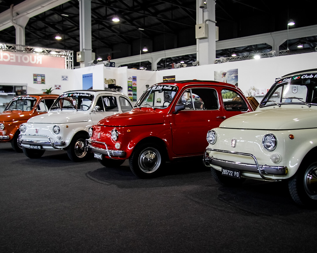 4 orange, white red and green FIAT 500 classic cars displayed in a salon
