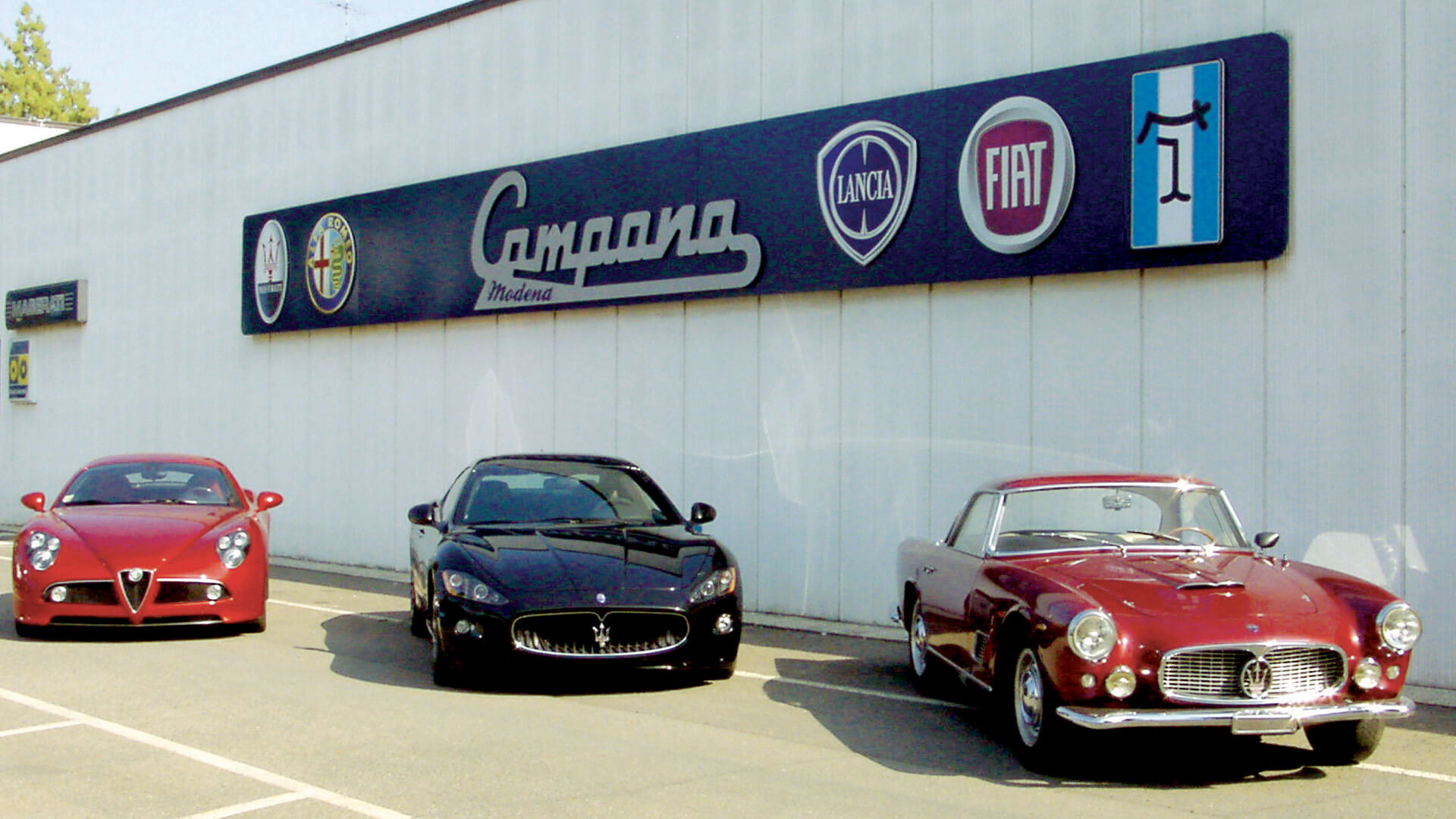 3 cars parked outside the Campana body shop in Modena, 1 red alfa romeo and 2 Maseratis one black and one red vintage