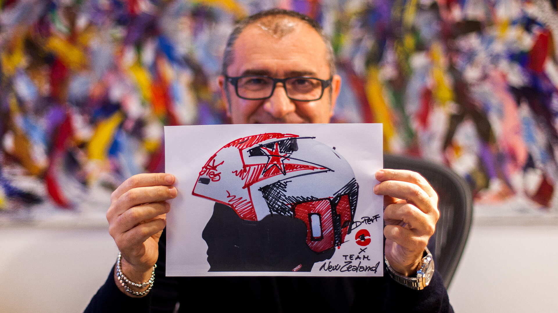 persona che tiene in mano un foglio con un disegno di un pilota con un casco e la scritta per il team new zealand