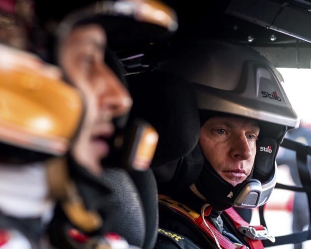 Two close-ups of two Iron Lynx drivers with helmets on, inside the cockpit of an endurance car, preparing to drive