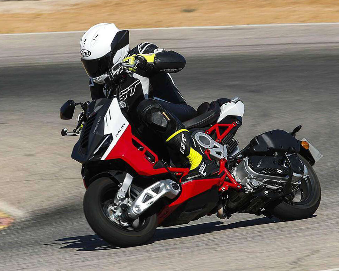 Racer in racing gear negotiating a curve riding a black white and red motorcycle processed by Italjet