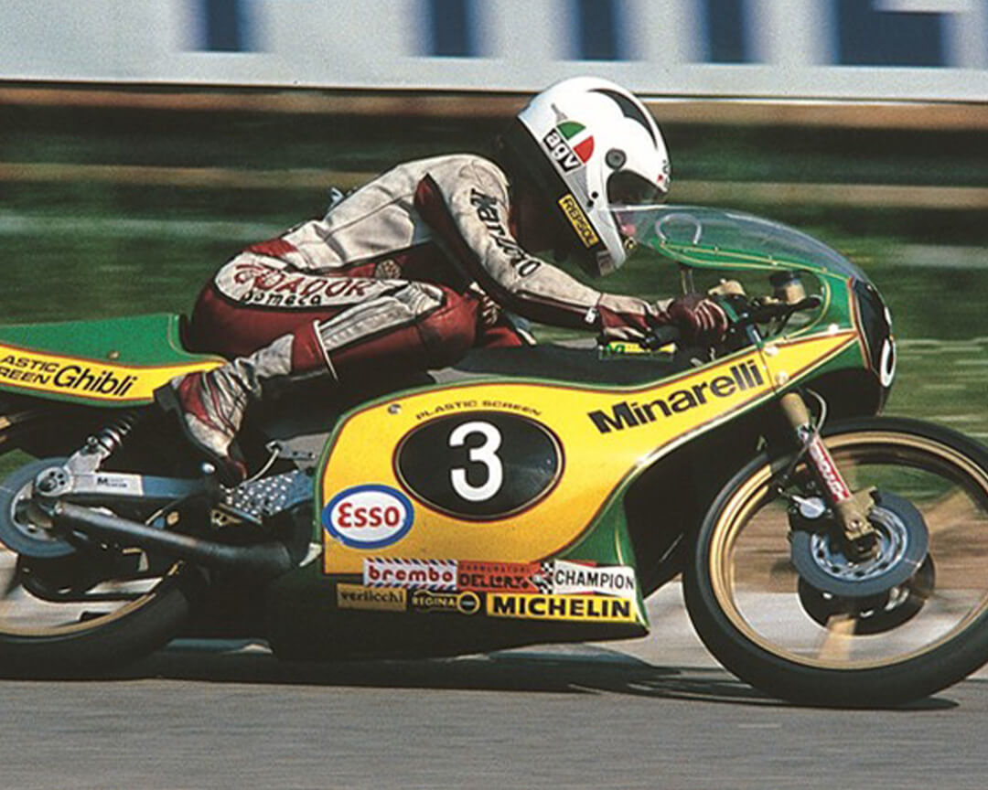 A vintage photo shows a rider riding a minarelli racing motorcycle in yellow and green livery, with the number three