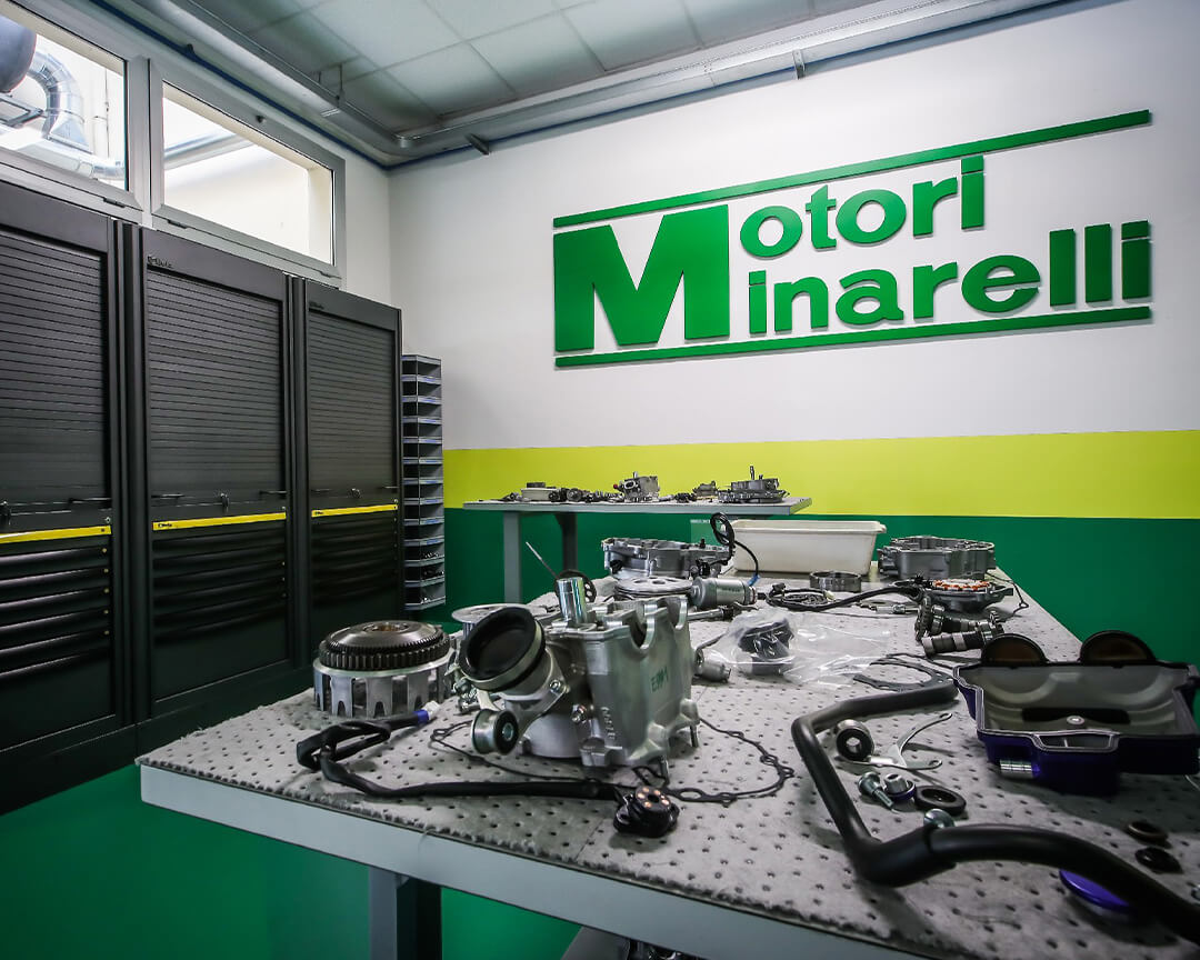 Inside the minarelli workshop on the work table, components of an engine under construction are resting, on the wall there is the motori minarelli logo